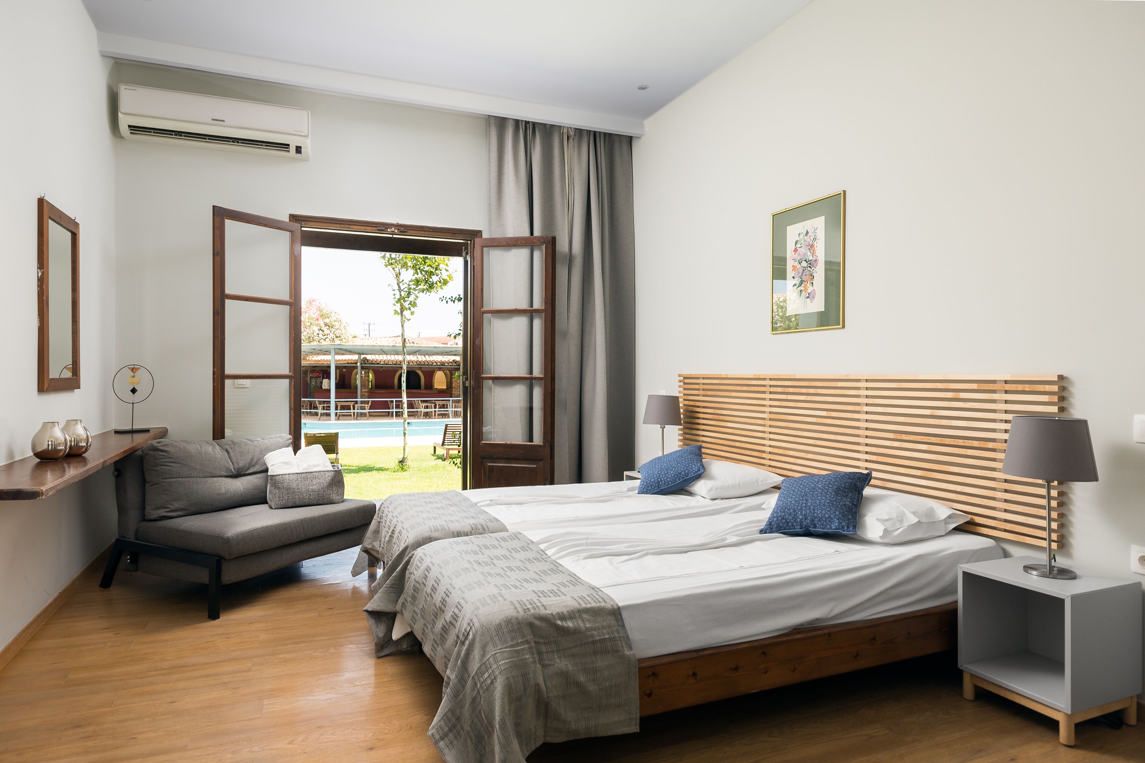 Une chambre d’hôtel avec un lit, un canapé, une table de chevet et une vue sur une piscine extérieure.