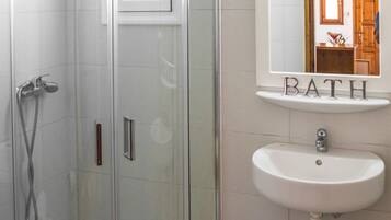 A bathroom with a glass-enclosed shower, a sink, and a mirror with the word "BATH" on it.