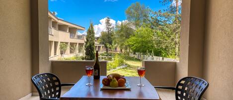 A balcony with a table set for two, featuring a bottle of wine, glasses, and a plate of fruit.