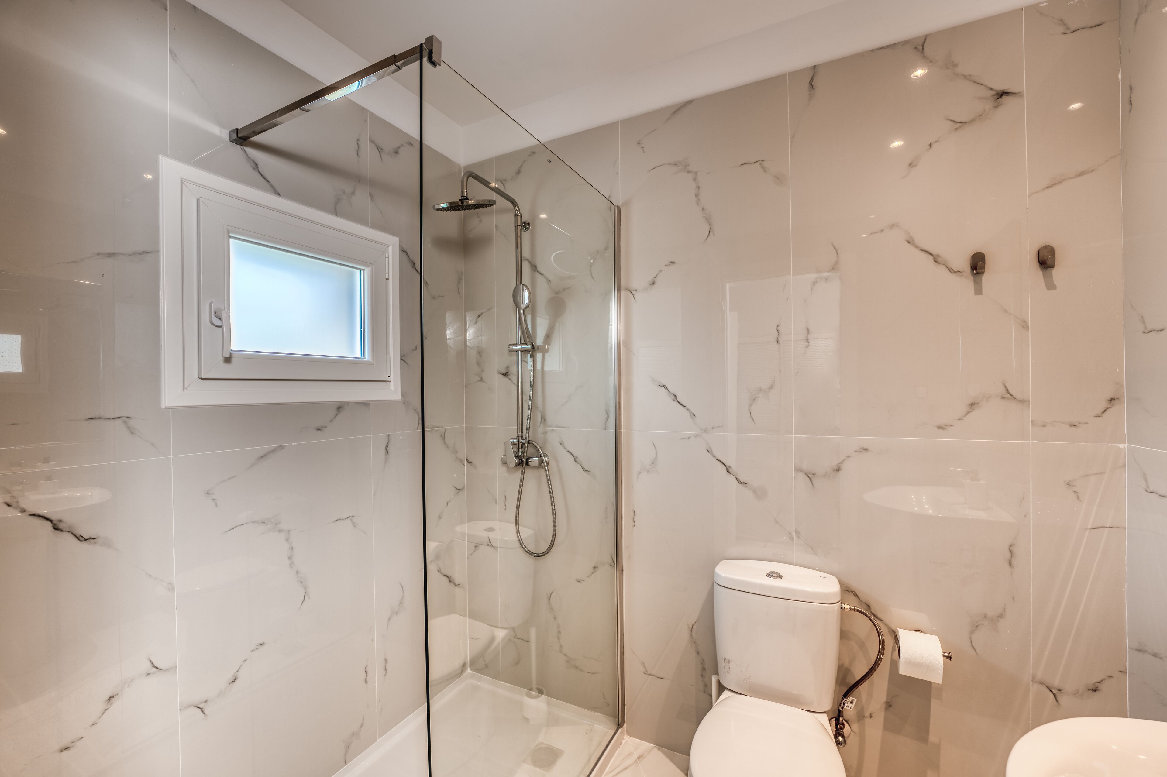Un baño moderno con ducha de vidrio, inodoro y pared con azulejos de mármol.