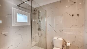 A modern bathroom with a glass-enclosed shower, a toilet, and a marble-tiled wall.