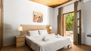 A bedroom with a wooden ceiling, a bed with white linens, a bedside table with a lamp, and a window with curtains. - Folies Corfu Hotel Apartments (Corfu)