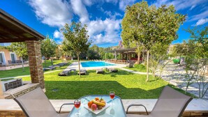 An outdoor patio with two chairs, a table with fruit and drinks, a pool, and a covered seating area. - Folies Corfu Hotel Apartments (Corfu)