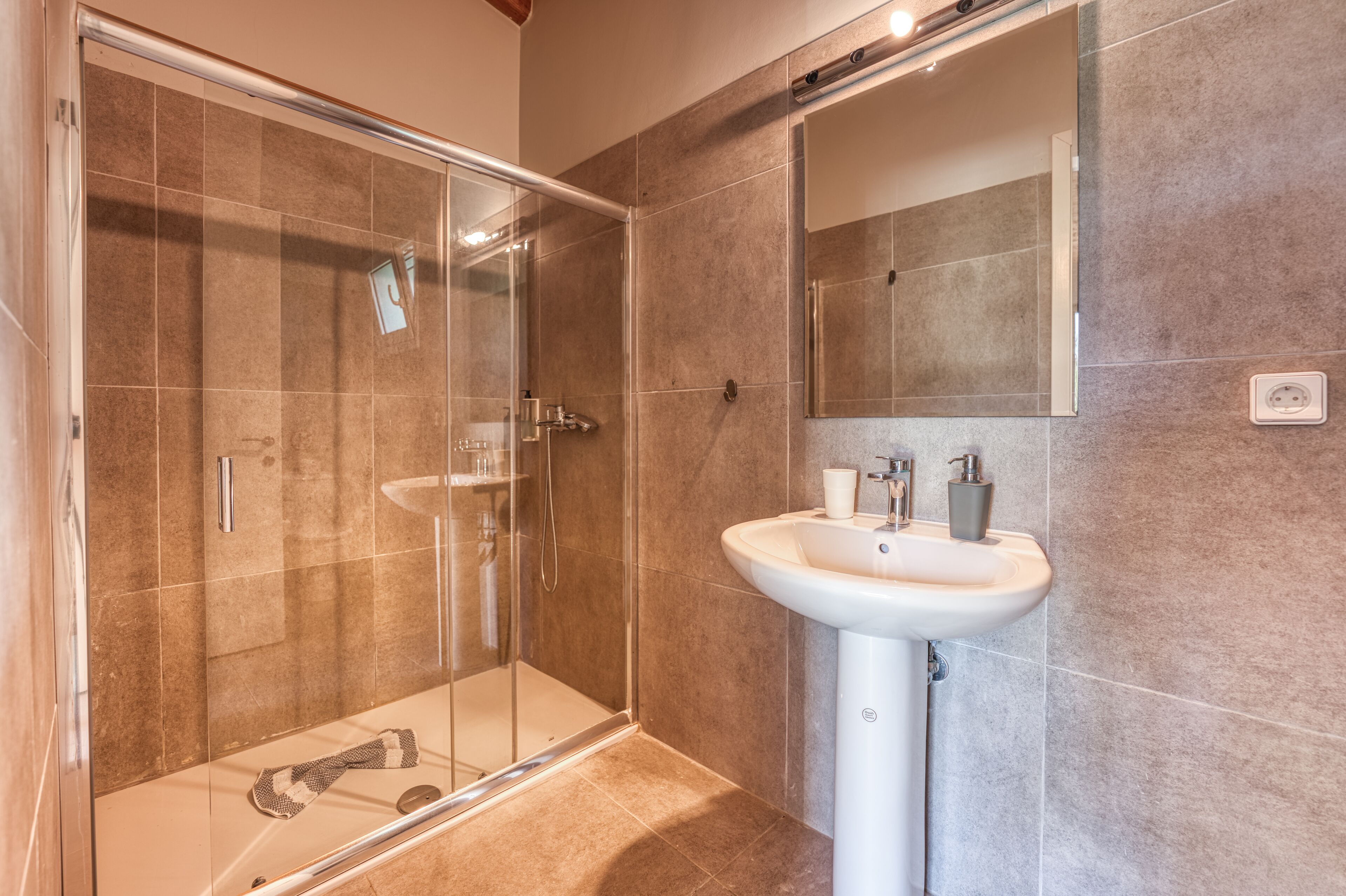 A modern bathroom with a glass-enclosed shower, a white sink, and a large mirror.