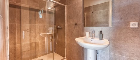 A modern bathroom with a glass-enclosed shower, a white sink, and a large mirror.