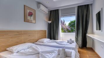 Une chambre d’hôtel avec deux lits, une tête de lit en bois, une fenêtre avec des rideaux, un tableau encadré et un appareil de climatisation.