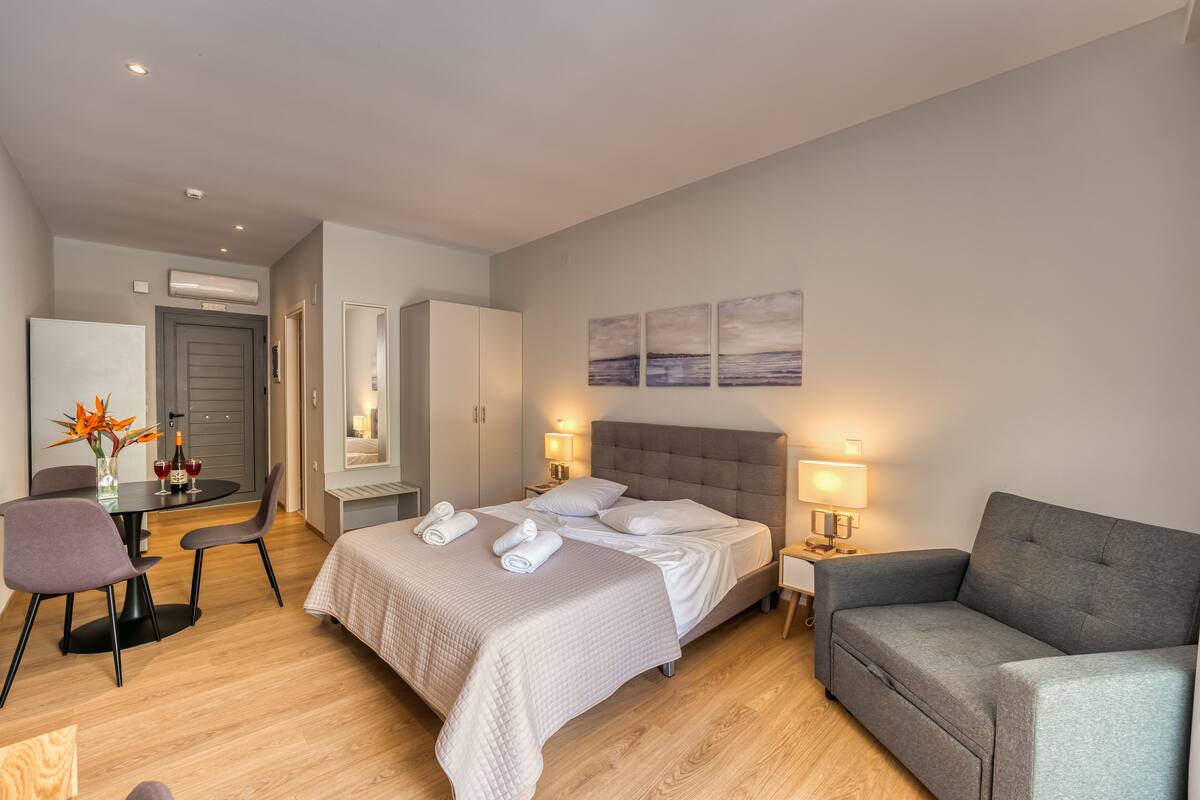 A modern hotel room with a bed, a sofa, a desk with a chair, and a dining table.