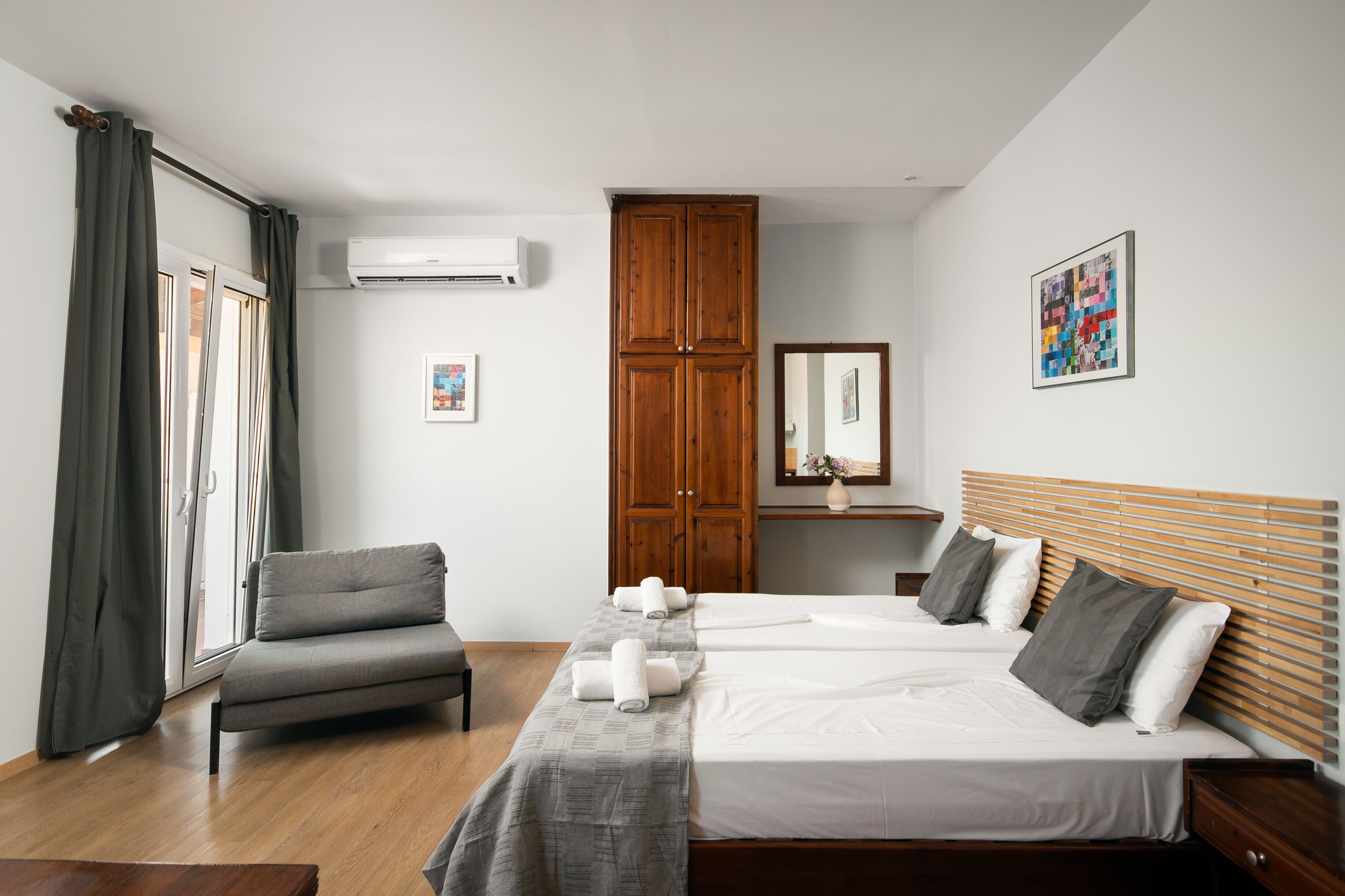 Habitación de hotel con dos camas, un sofá, un armario de madera, aire acondicionado y un cuadro en la pared.