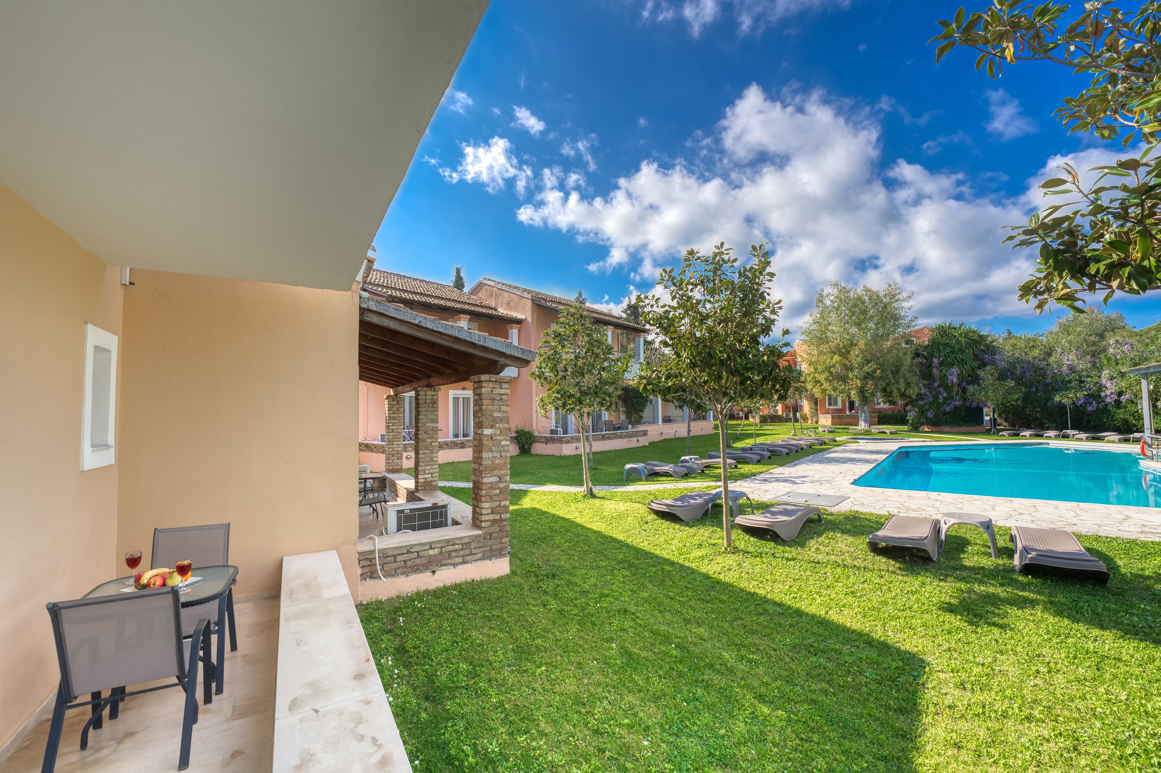 Un área junto a la piscina con mesa y sillas, piscina y un edificio con tejado de baldosas.