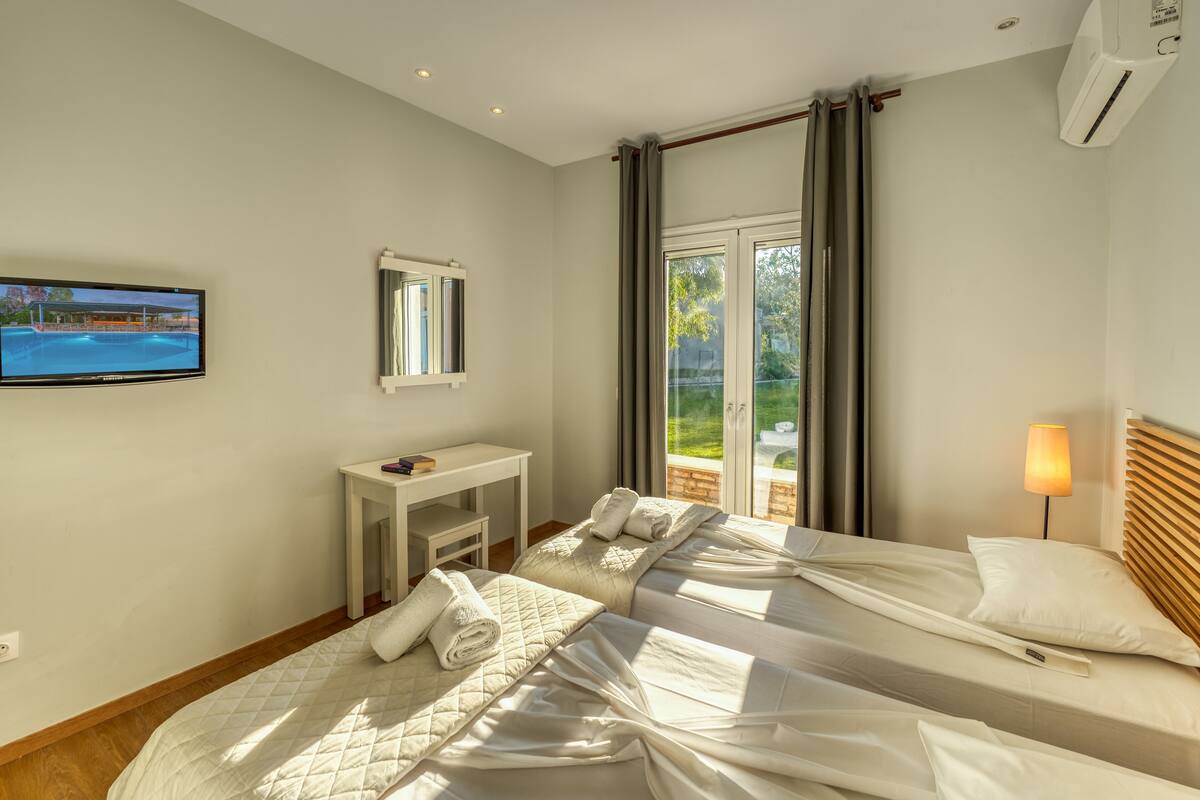 A hotel room with two beds, a TV, a desk, and a view of a pool.