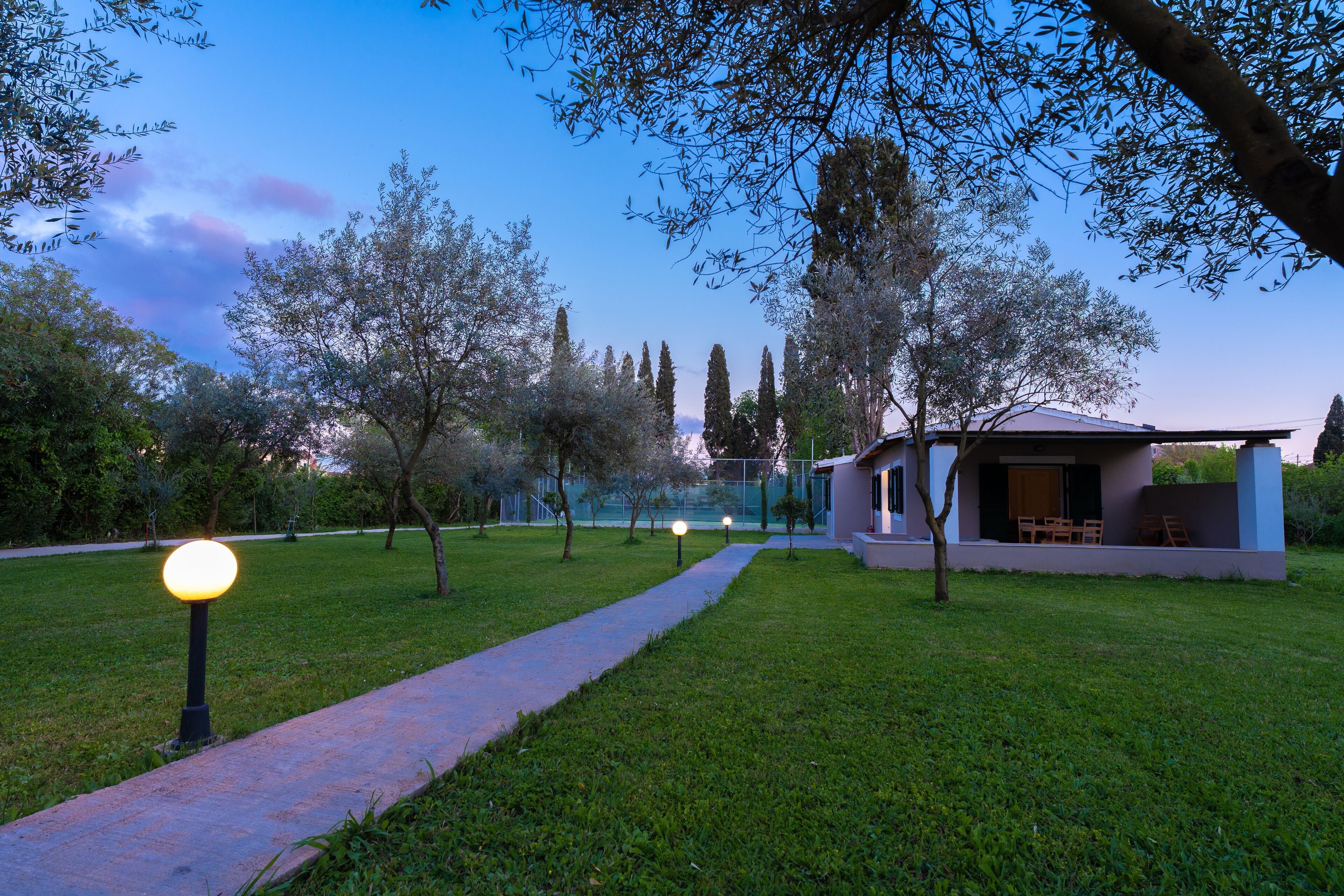 Un camí que condueix a una casa moderna amb façana de vidre, envoltada d'arbres i un jardí ben cuidat.