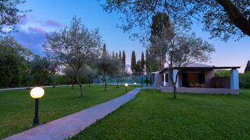 Un camí que condueix a una casa moderna amb façana de vidre, envoltada d'arbres i un jardí ben cuidat.