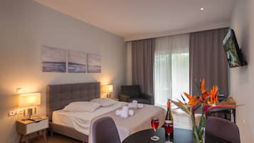 Une chambre d’hôtel comprenant un lit, des tables de chevet, un bureau, une chaise, une table à manger avec des verres à vin et un vase à fleurs.