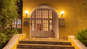 A hotel entrance with a grand arched doorway, a stone staircase, and two illuminated signs indicating the hotel name. - Folies Corfu Hotel Apartments (Corfu)