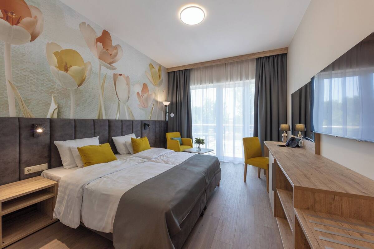 Ein Hotelzimmer mit einem großen Bett, einem Schreibtisch, einem Sessel und einem großen Fenster mit Vorhängen.