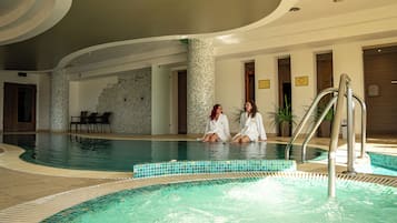 Una piscina interior con dos personas sentadas al borde, rodeada de paredes de azulejos y un diseño moderno.