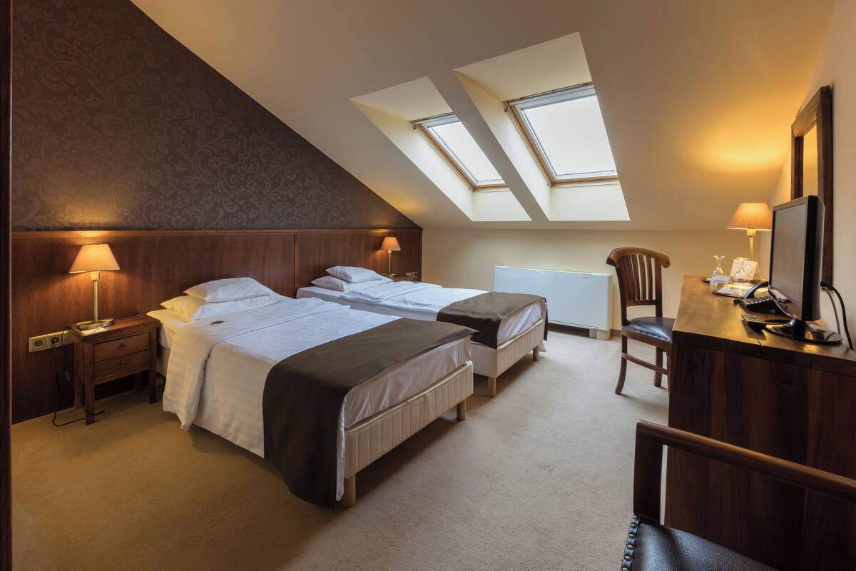Ein Hotelzimmer mit zwei Betten, einem Schreibtisch, einem Stuhl und Dachfenstern.