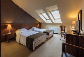 A hotel room with two beds, a desk, a chair, and skylights.