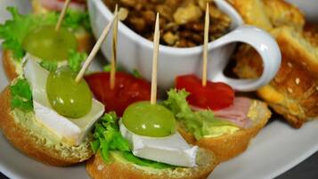 A plate with three open-faced sandwiches topped with cheese, lettuce, and a green grape, accompanied by a bowl of nuts and a slice of tomato.