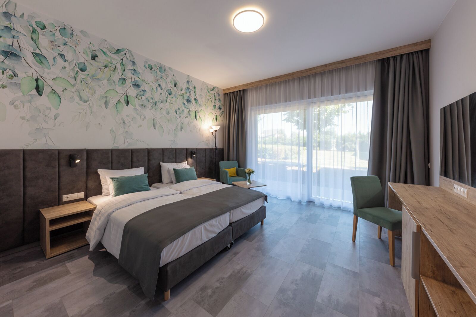 Ein modernes Hotelzimmer mit einem großen Bett, einem Schreibtisch, einem Stuhl, einem Nachttisch und einer Wand mit einem Blattmuster.
