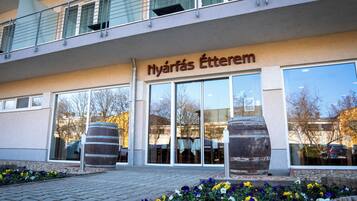A building with a sign reading "Nyárfás Étterem" and large windows reflecting trees and a car.