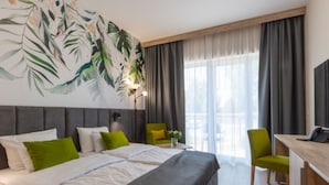 A hotel room with a large bed, a desk, and a chair. There is a window with curtains and a view of the outside.