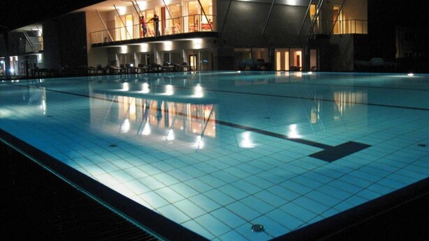 A swimming pool with a tiled deck and a building with multiple windows in the background.