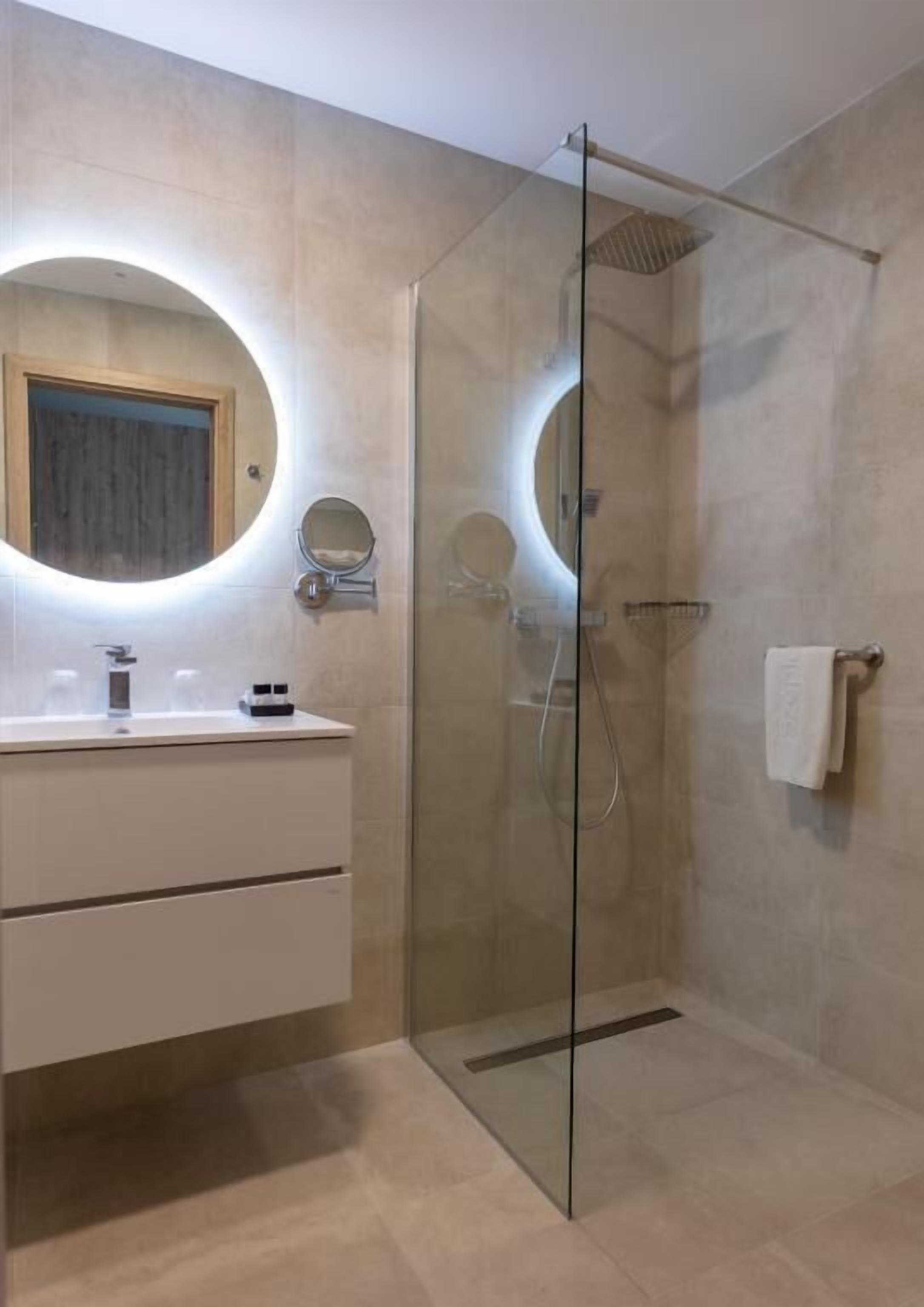 A modern bathroom with a glass-enclosed shower, a round mirror, and a white vanity.