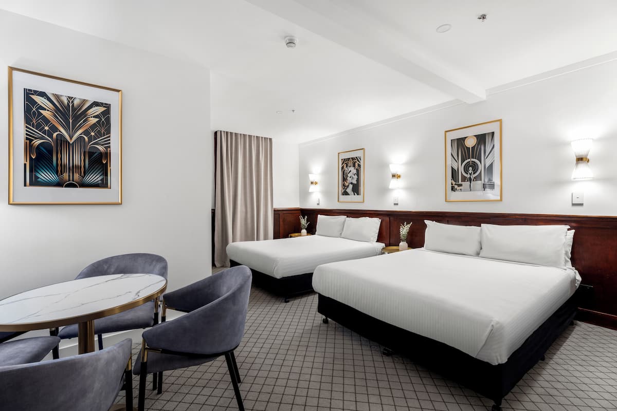 Et hotelværelse med to senge, et rundt bord og to stole.