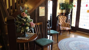 Un escalier en bois, une chaise en bois avec un coussin, une table en bois ornée d’un vase de fleurs et un tapis à motifs.