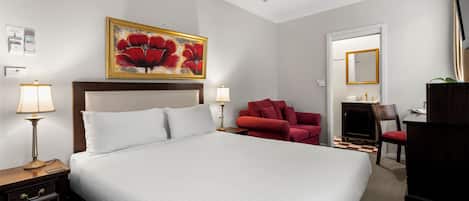 A hotel room with a large bed, two bedside tables with lamps, a red armchair, a desk with a chair, a television, and a ceiling fan.