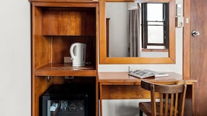 Un bureau compact en bois, accompagné d’une chaise, d’une bouilloire, d’un petit réfrigérateur et d’un miroir.