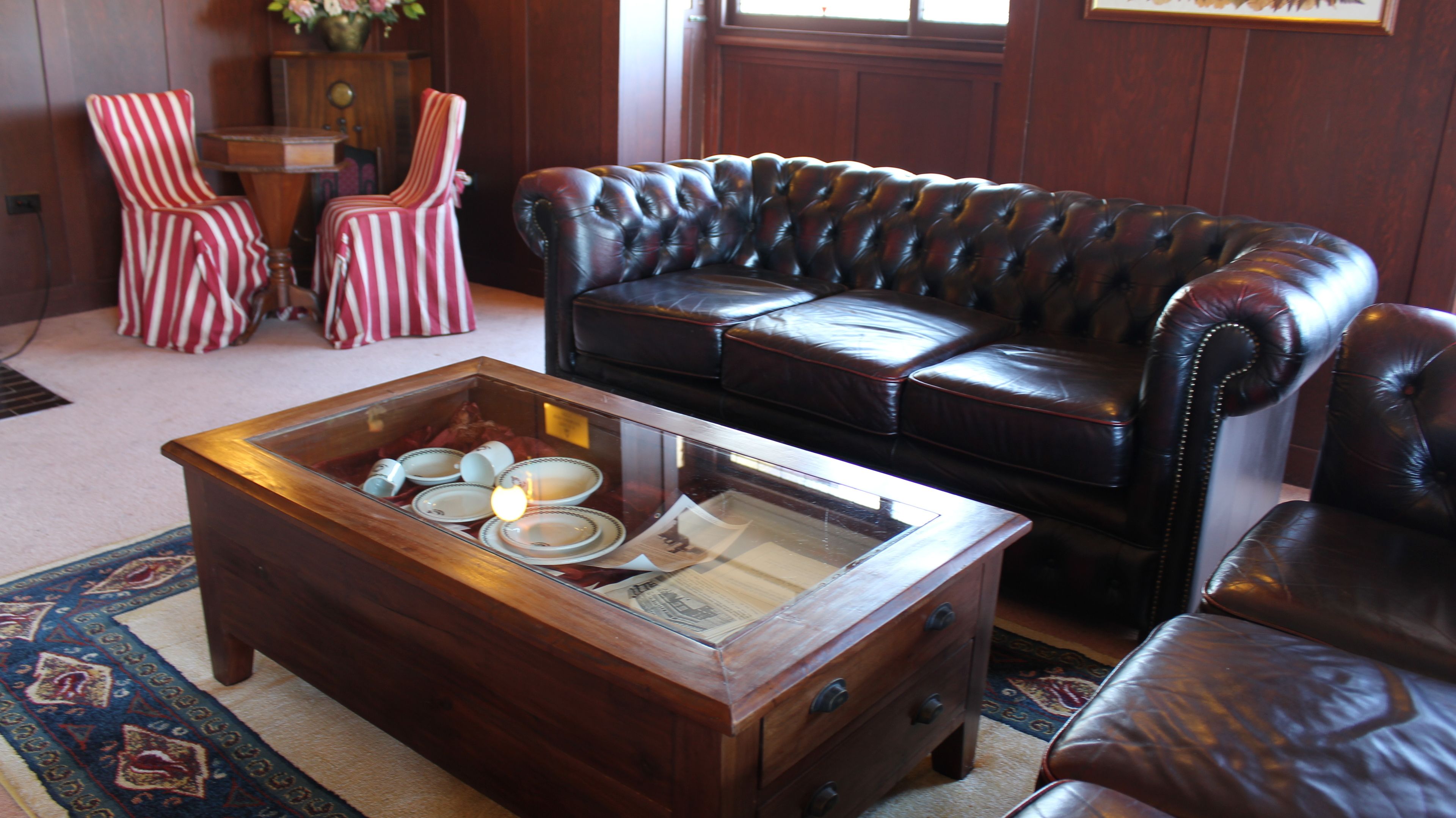 Een woonkamer met een leren bank, gestreepte stoelen en een houten salontafel met servies.