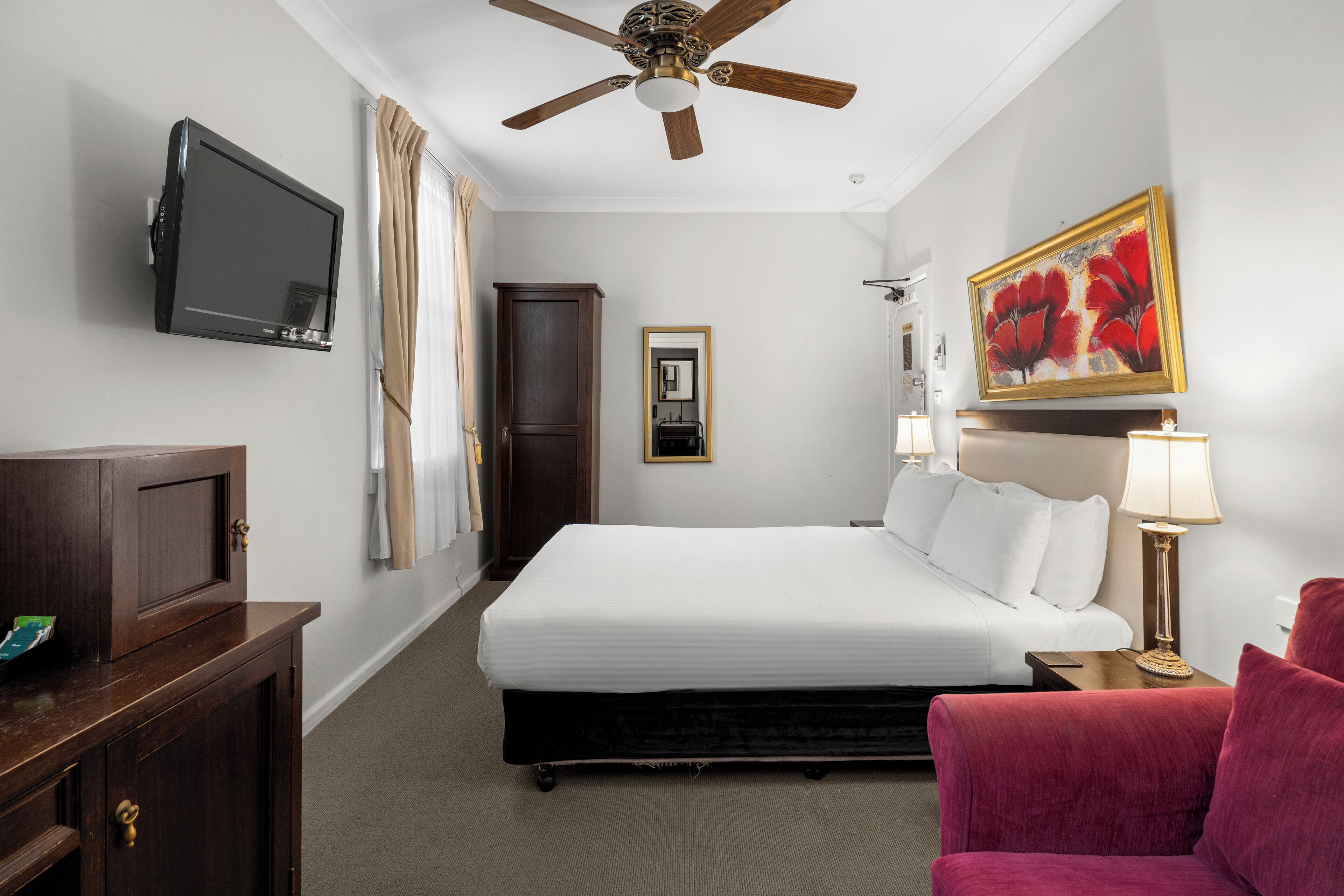 Habitación de hotel con cama, televisión, ventilador de techo, un cuadro, lámpara y una silla.