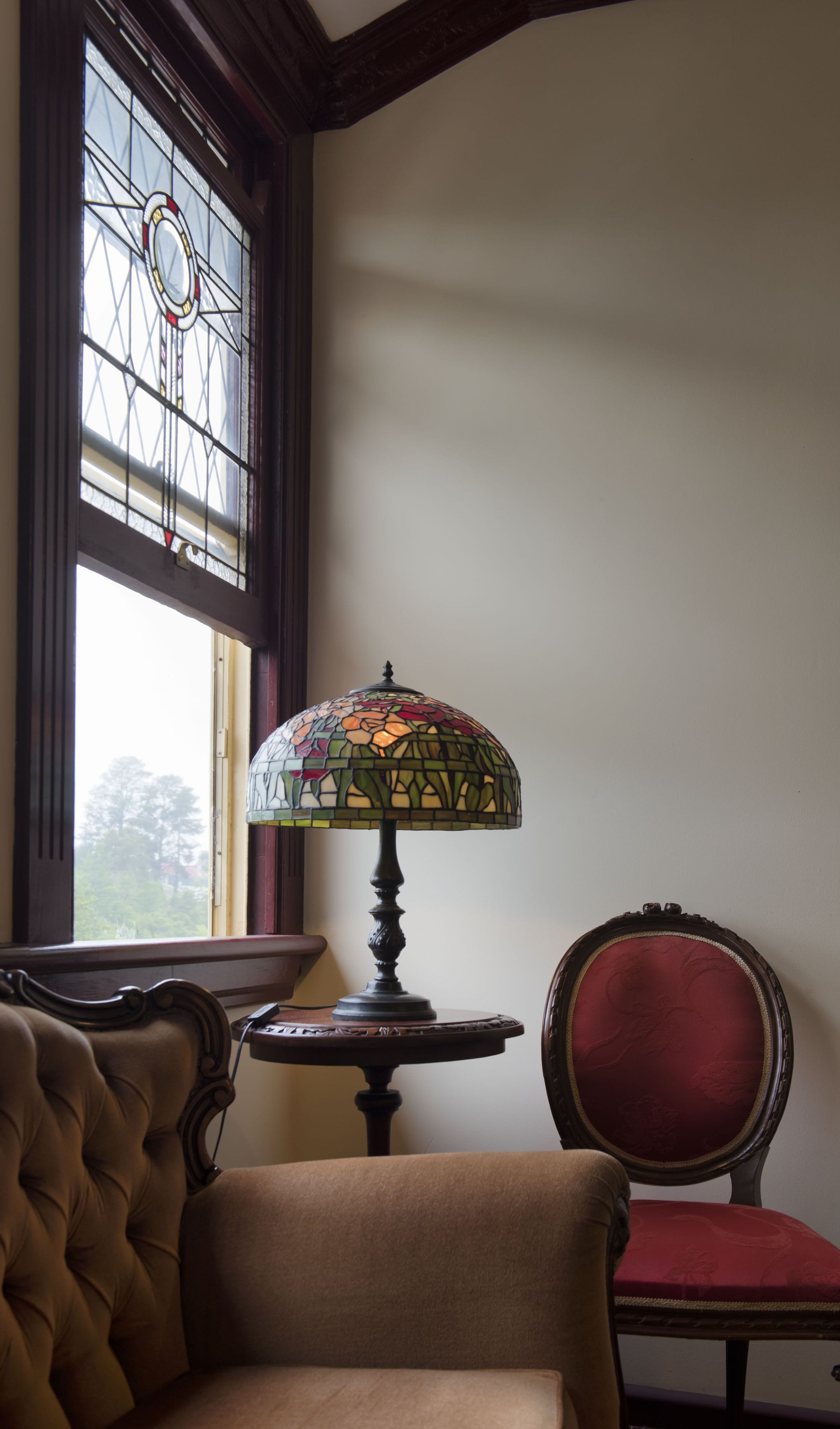 Et værelse med et farvet glasvindue, en bordlampe, en stol og en polstret lænestol.