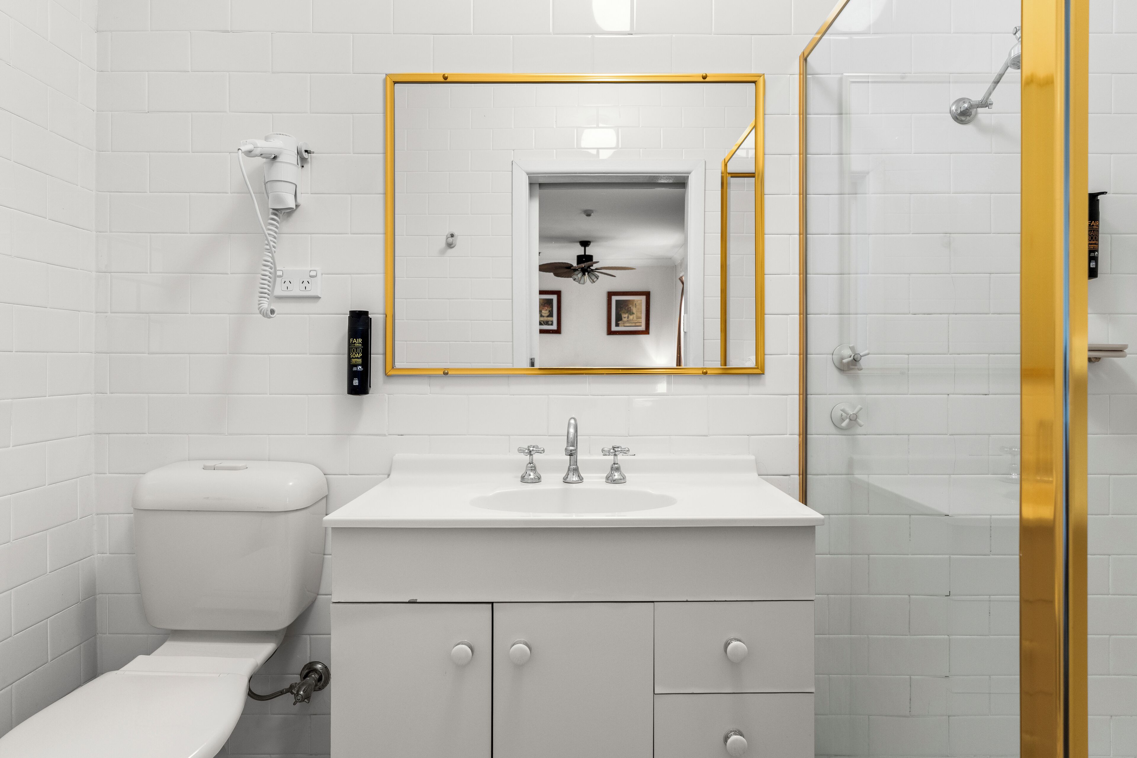 A modern bathroom with a white toilet, a sink with a gold-framed mirror, and a shower area.