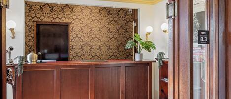 A reception desk with a patterned wallpaper backdrop, a potted plant, and a sign indicating an excellent rating.