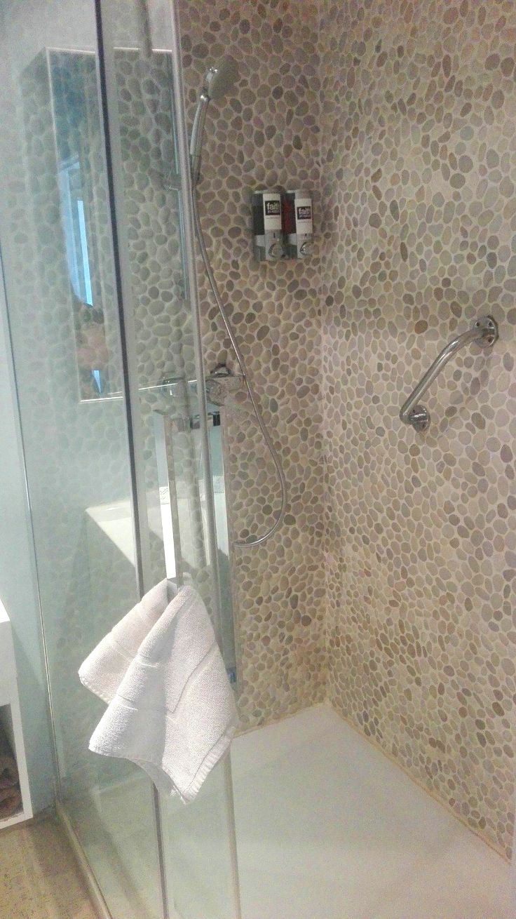 A glass-enclosed shower with a pebble-textured wall, a handheld showerhead, and a white towel hanging on the glass door.