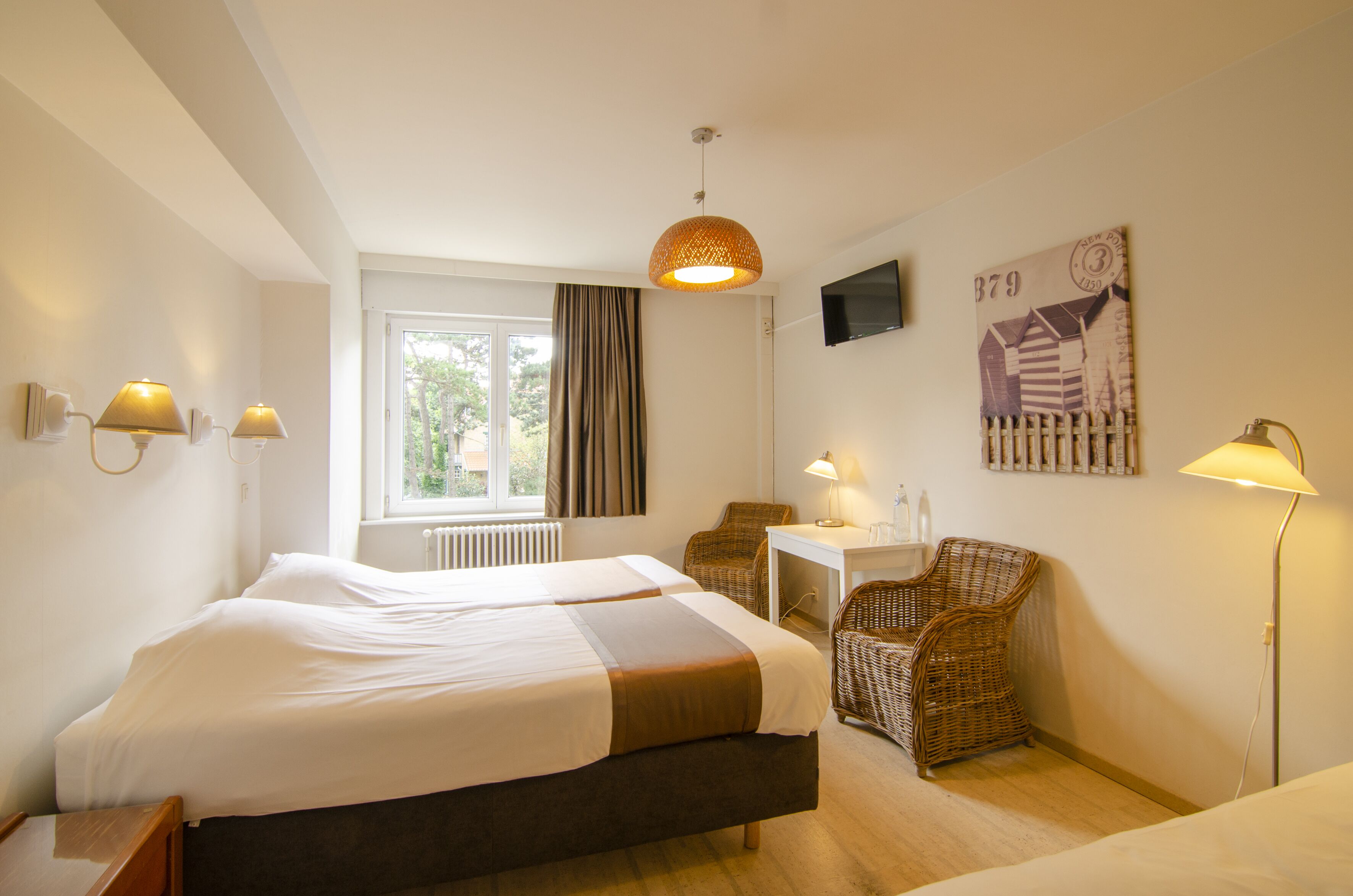 Een hotelkamer met twee bedden, een bureau, rieten stoelen en een televisie aan de muur.