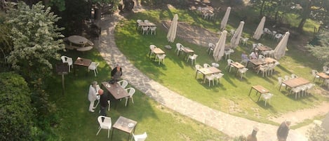 Un patio al aire libre con varias mesas y sillas, rodeado de follaje y árboles.