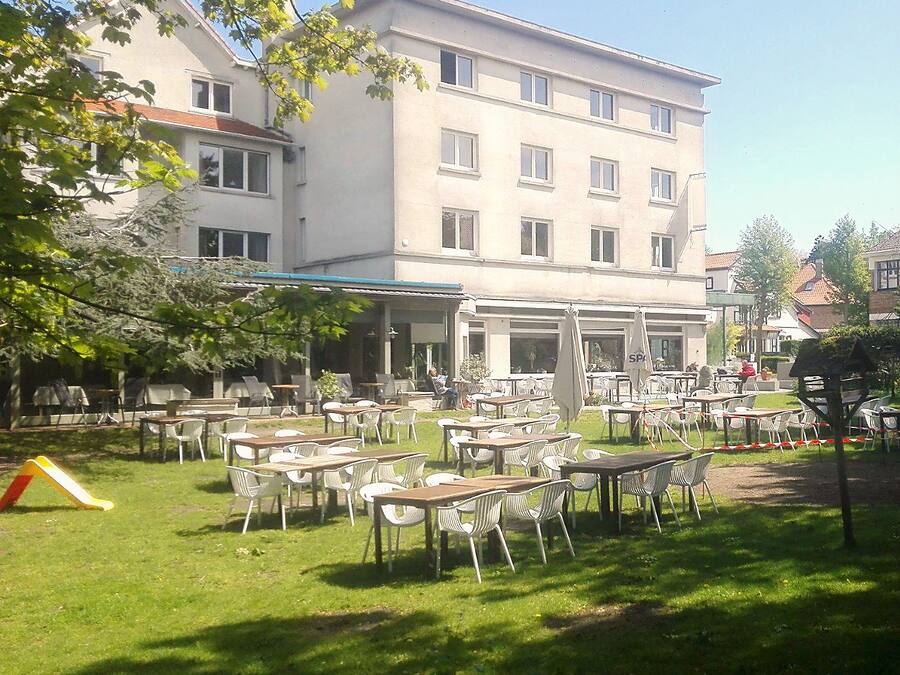 Een terras met tafels en stoelen, een speeltuin en een gebouw met meerdere ramen en balkons.