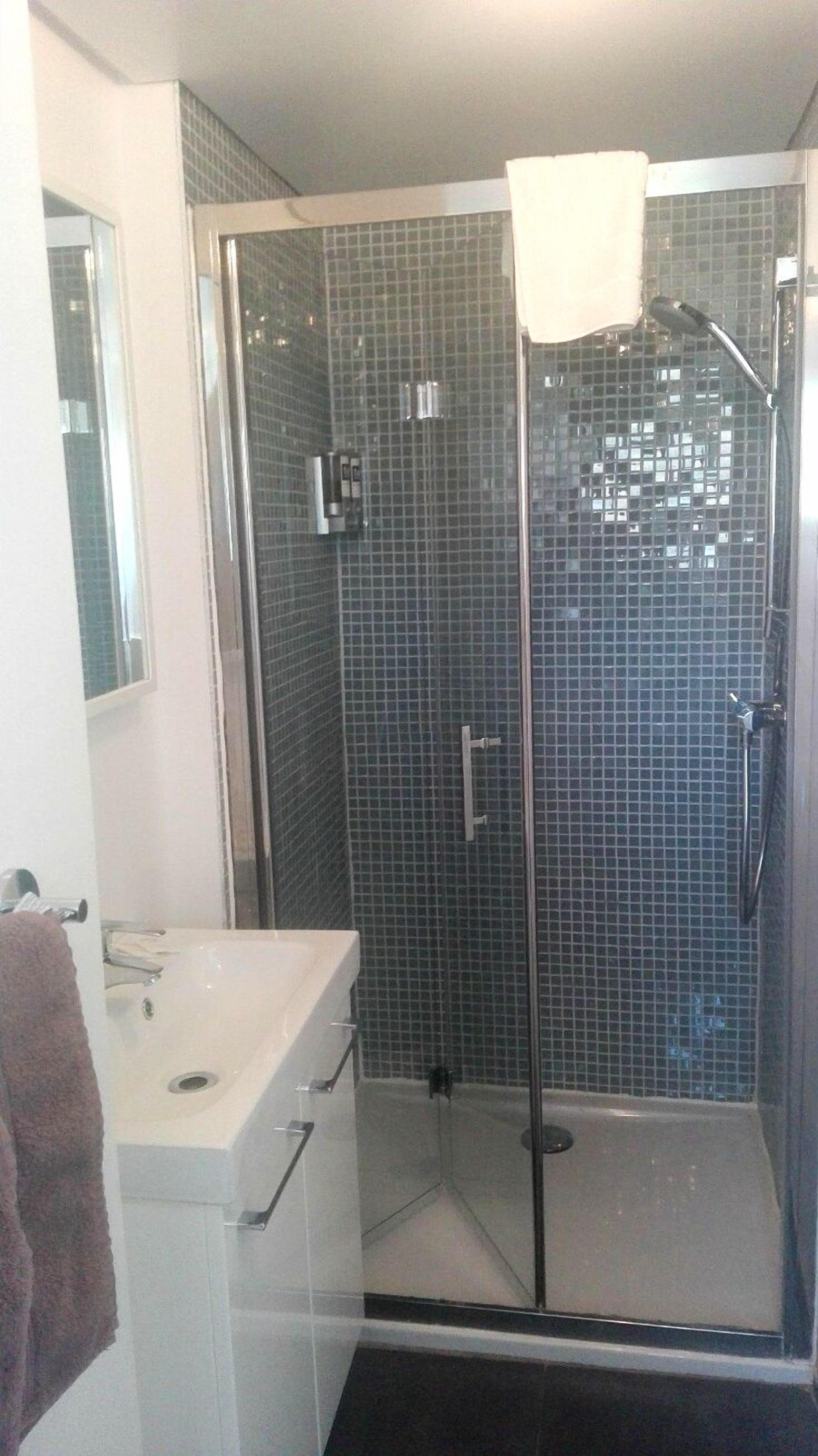 A shower with a glass door, a white sink, and a mirror.