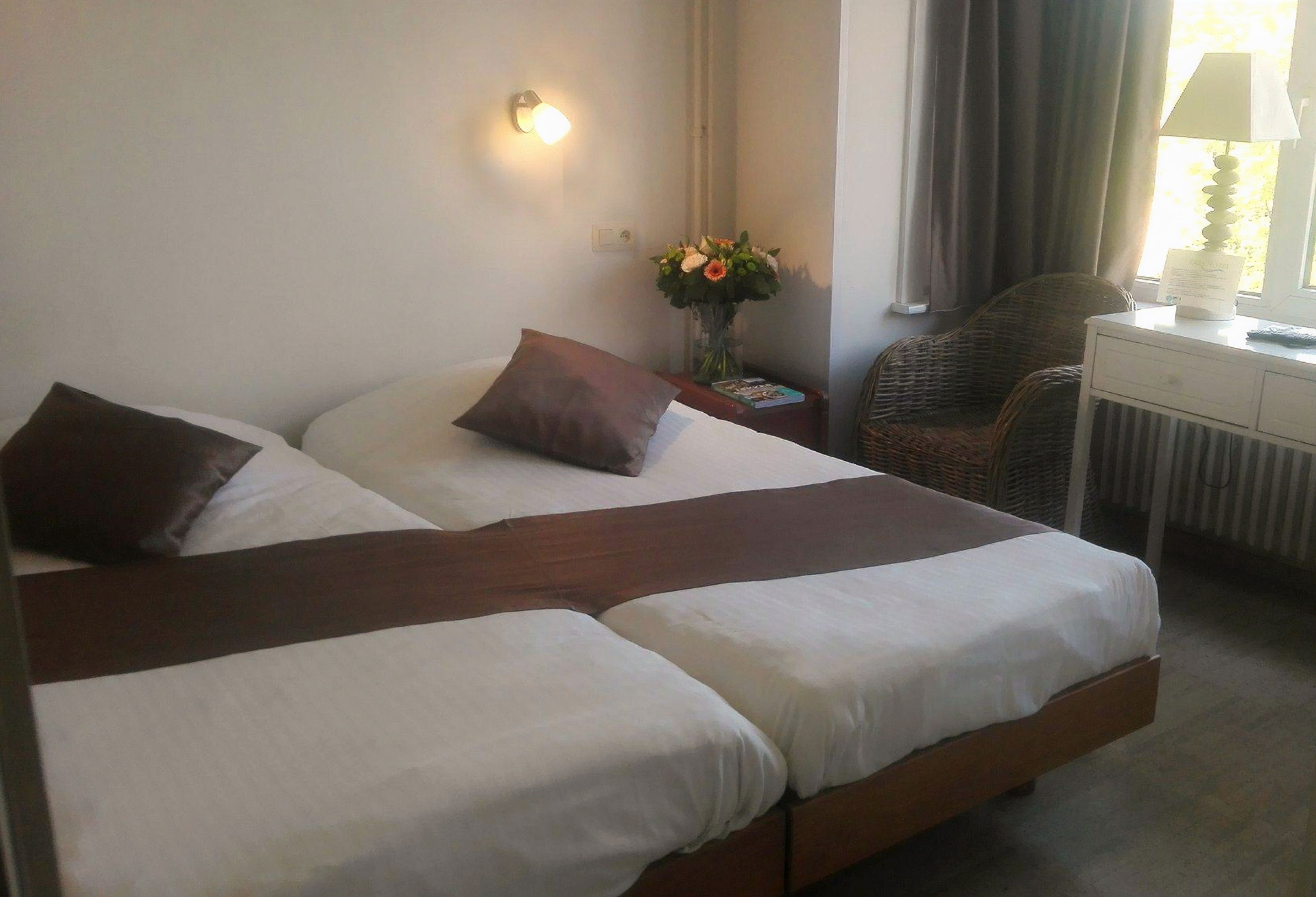 Ein Hotelzimmer mit einem großen Bett, einem Nachttisch mit Lampe, einem Sessel und einer Vase mit Blumen.