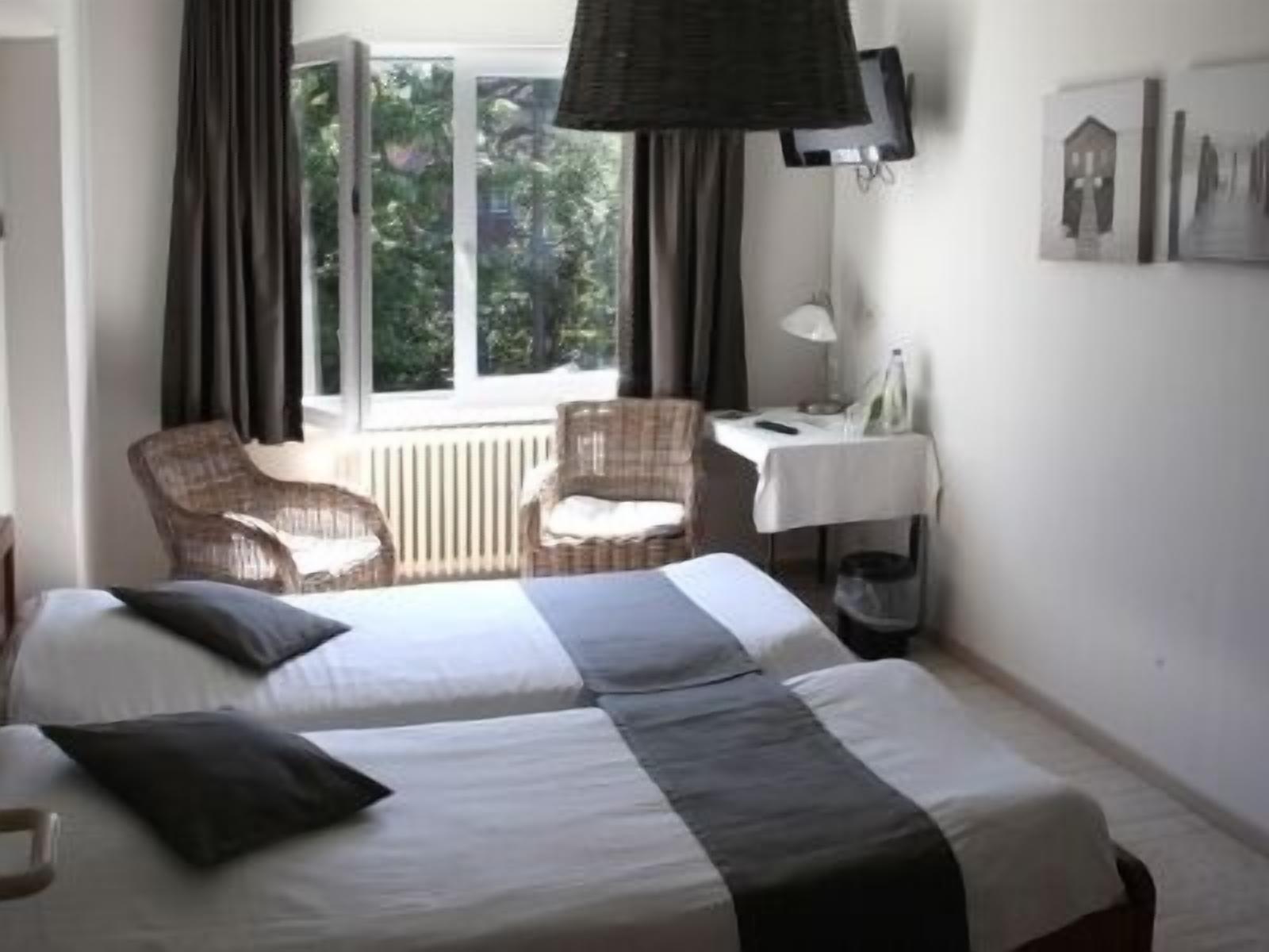 A hotel room with two beds, a chair, a table, and a window with curtains.