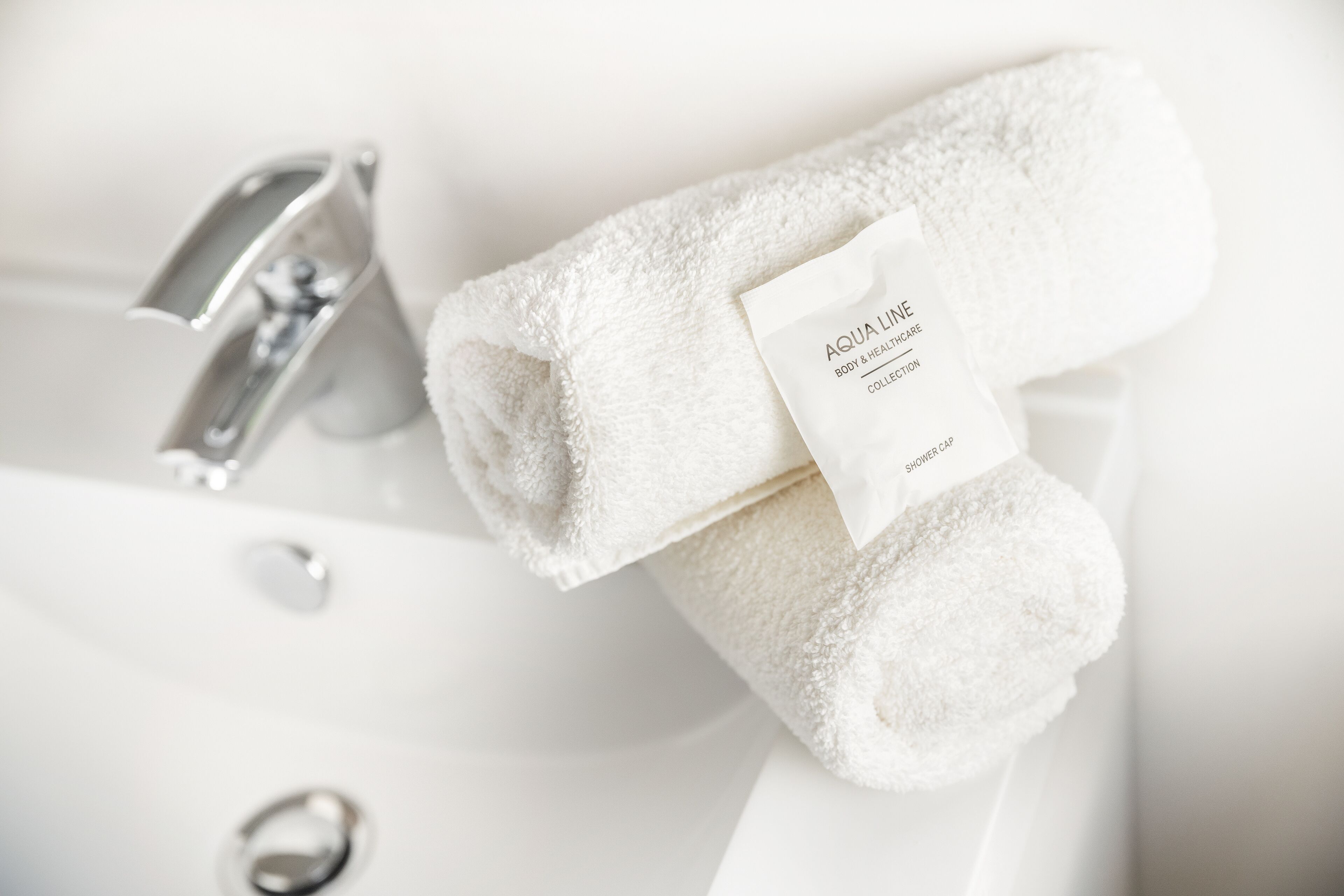A white bathroom sink with a towel and a label that reads "AQUA LIME BODY & HEALTH CARE COLLECTION."