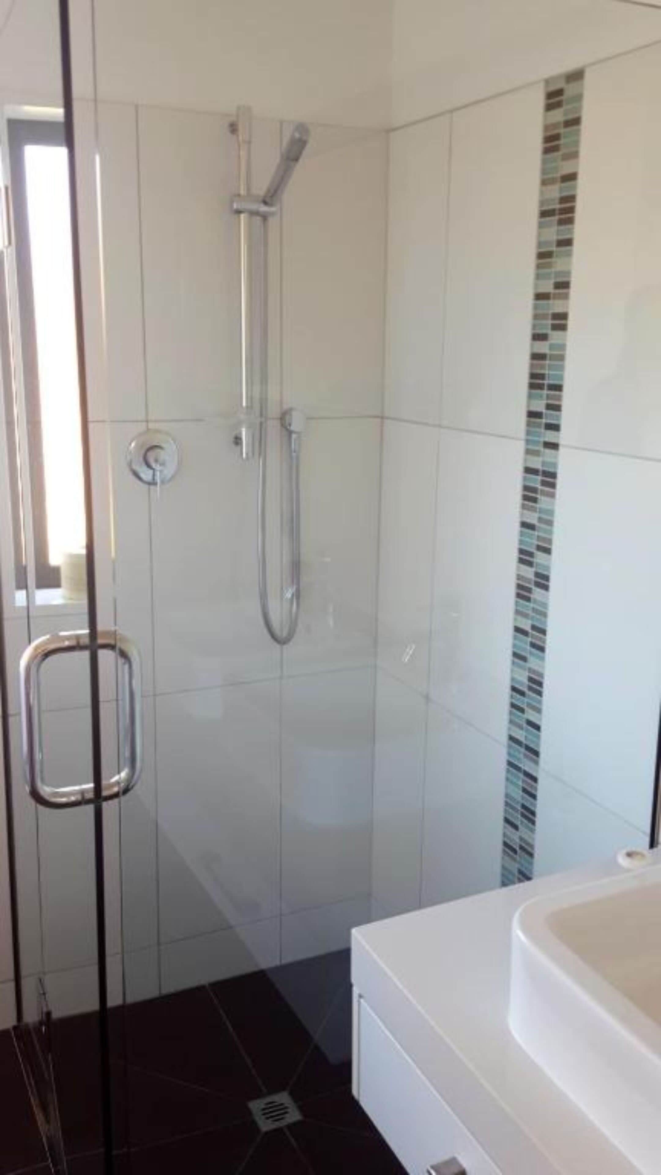 A modern bathroom with a glass shower enclosure, a white bathtub, and a tiled floor.