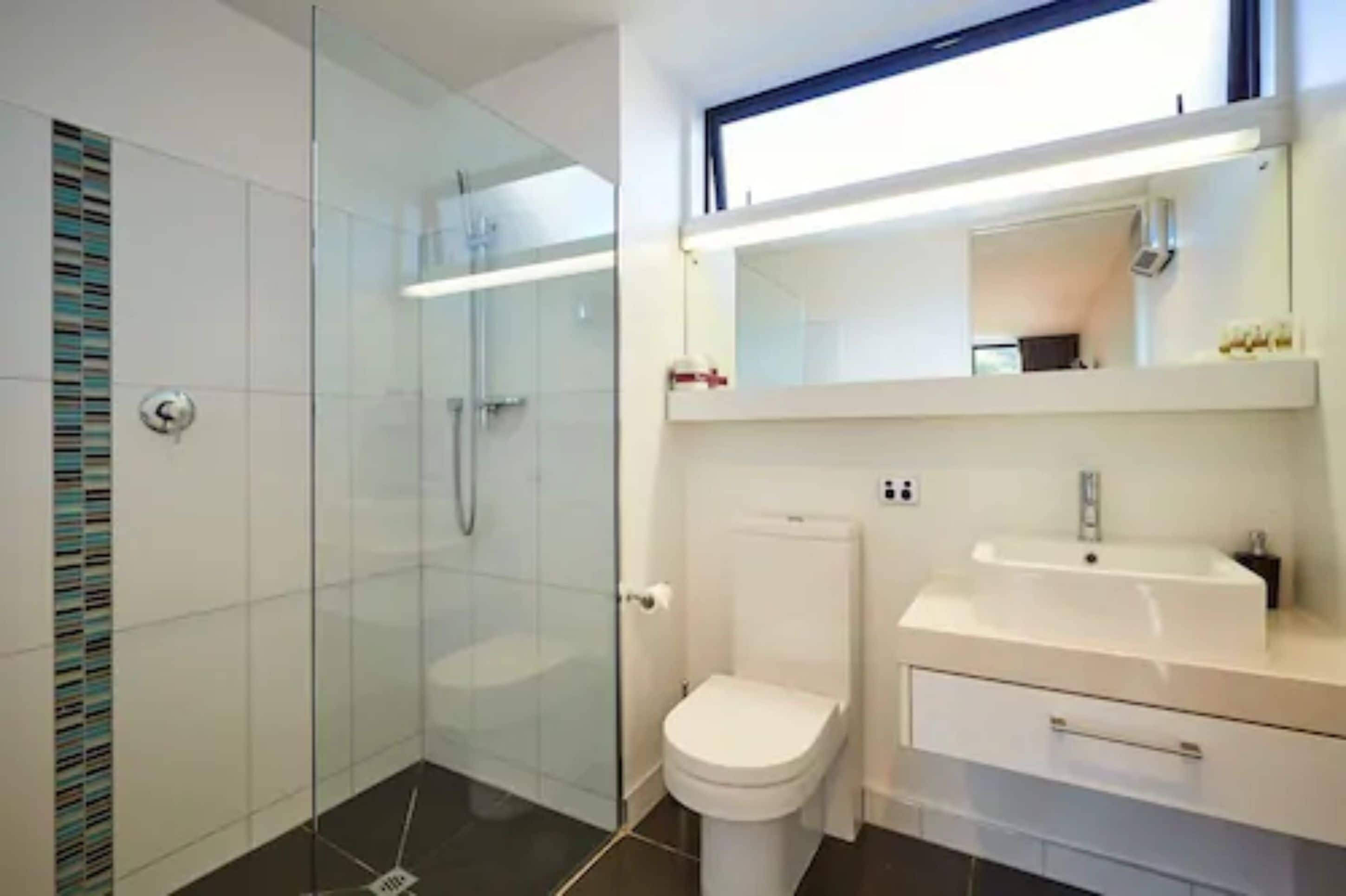 A modern bathroom with a glass shower enclosure, a white toilet, and a white sink with a mirror above it.