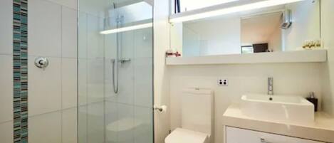 Un baño moderno con cabina de ducha de vidrio, inodoro blanco y lavamanos blanco con espejo sobre él.