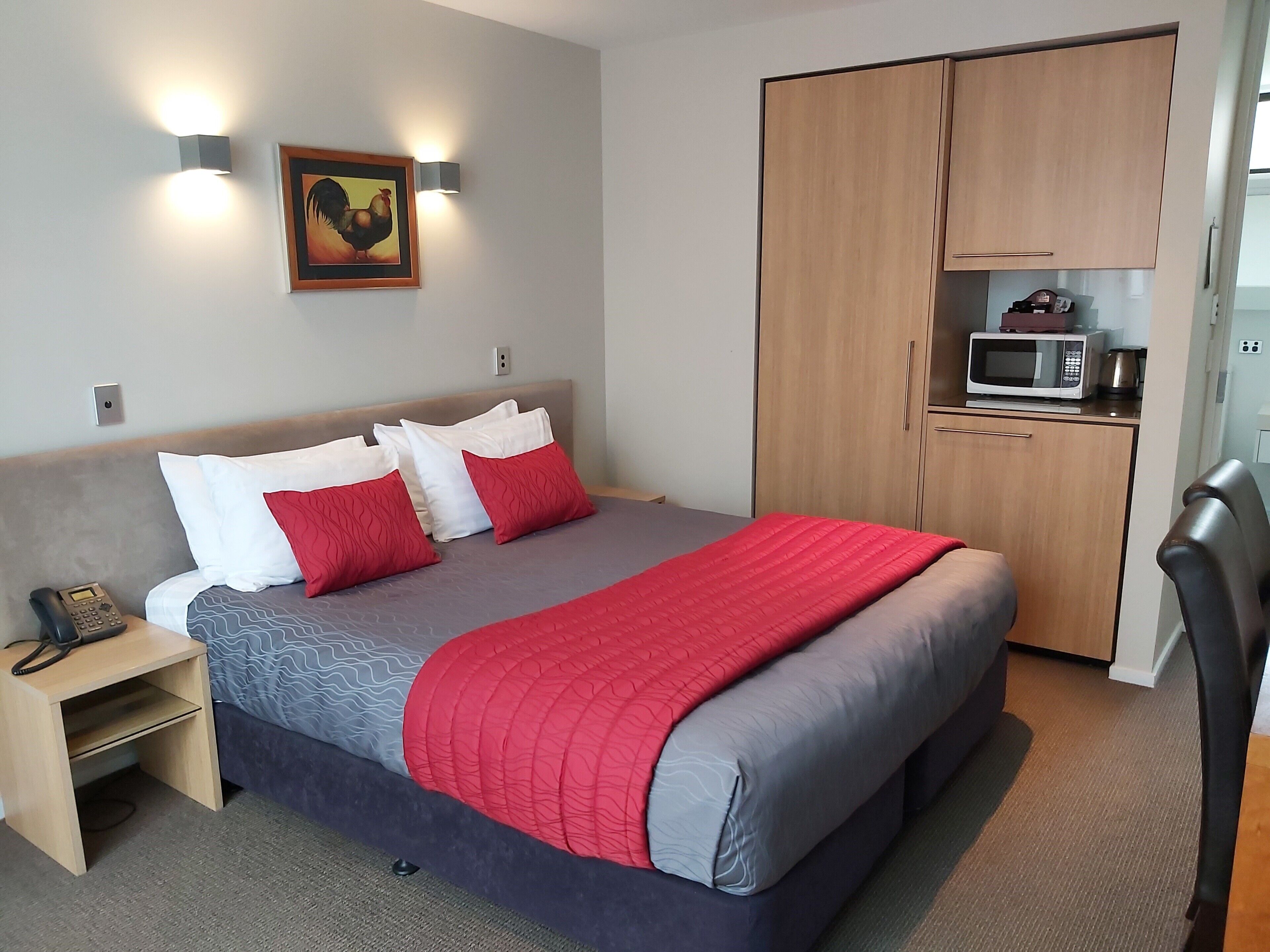 A hotel room with a bed, bedside table, lamp, and a wardrobe with a microwave.