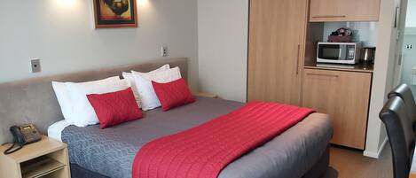 A hotel room with a bed, bedside table, lamp, and a wardrobe with a microwave.